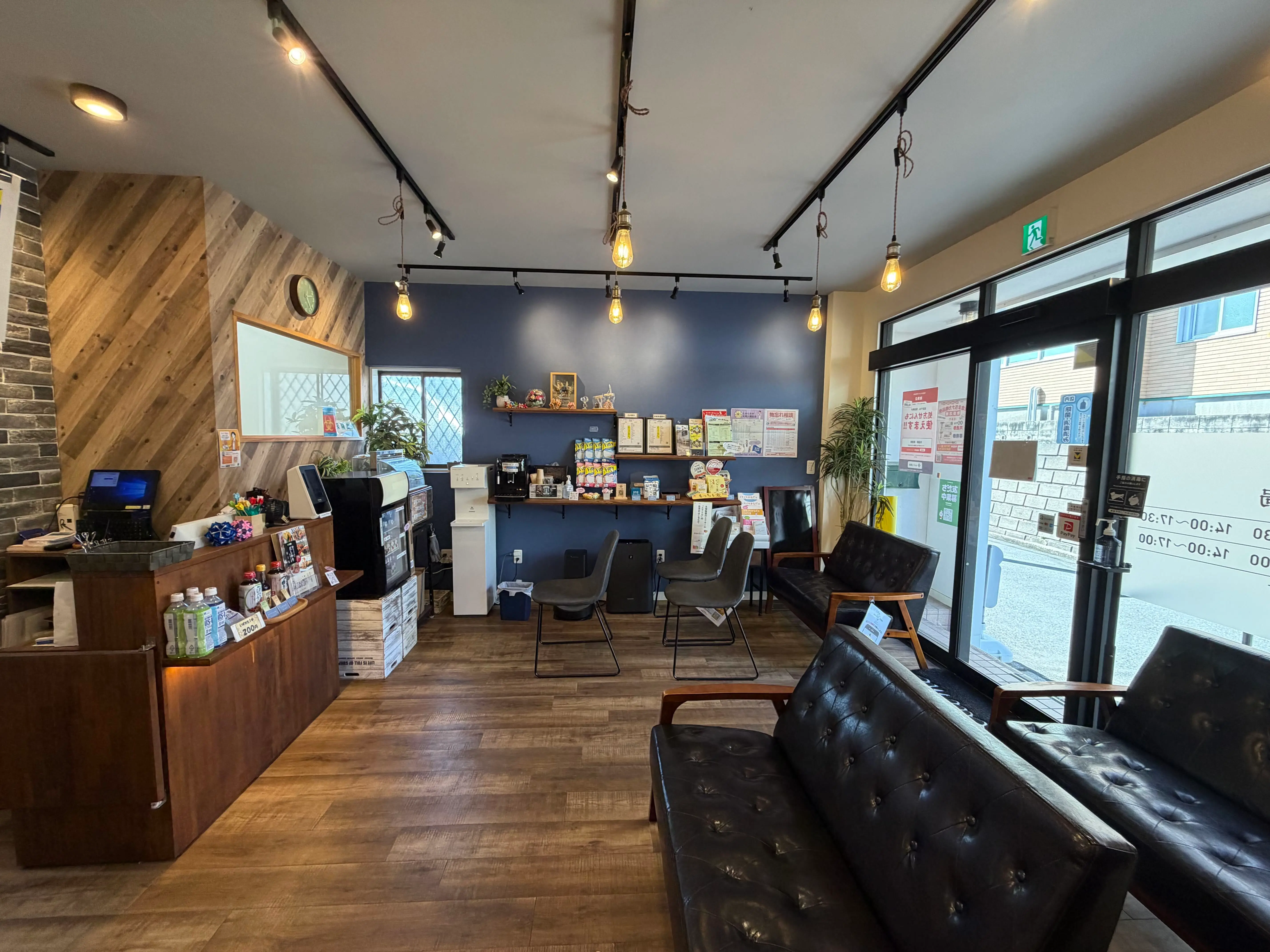 佐倉店の待合。紺色の壁に電球がさがり、窓際に革のソファと椅子が並んでいる